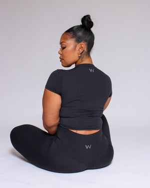 Person wearing a black outfit with a logo, sitting on a white background