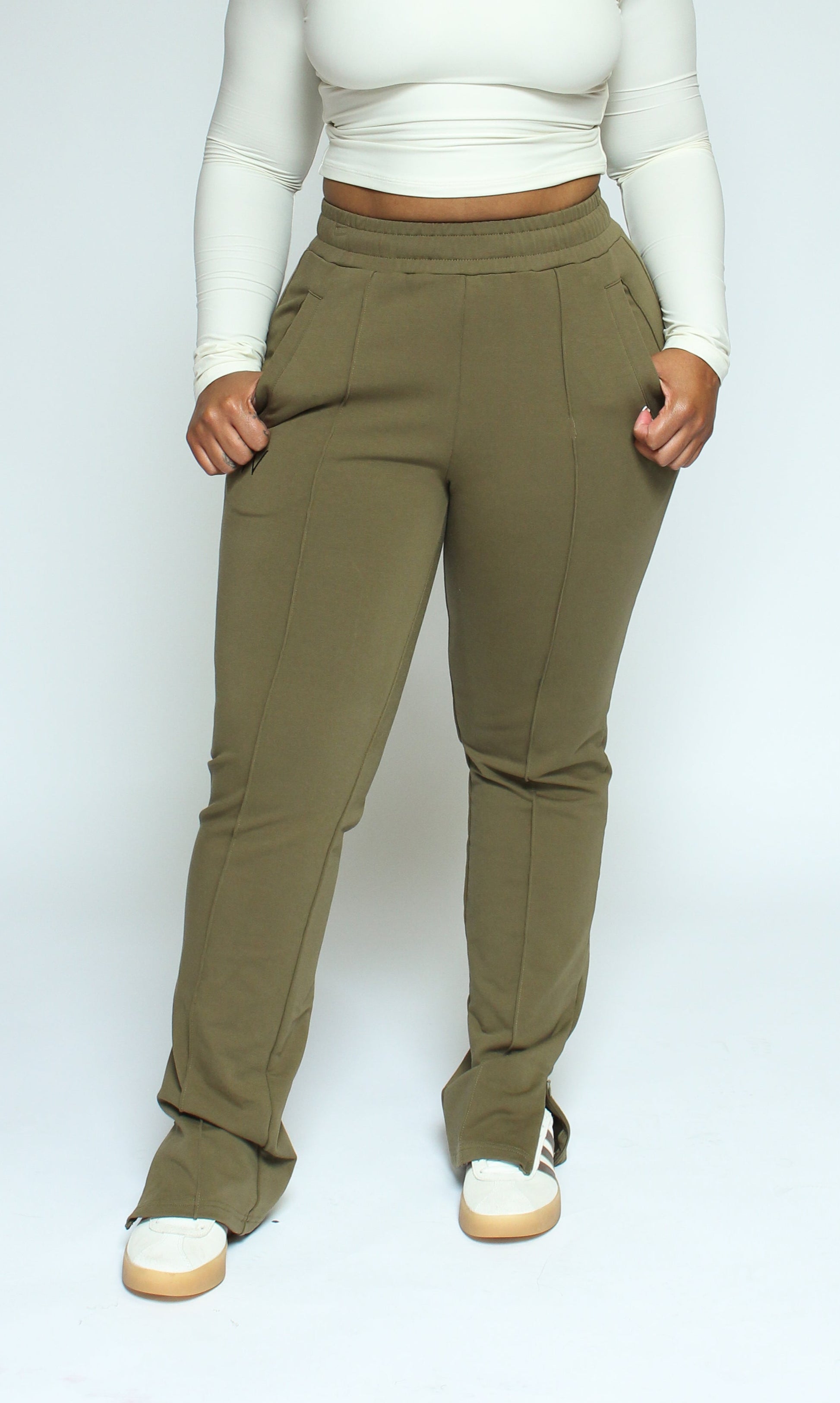 Woman wearing a white long-sleeve top and olive green pants against a plain background