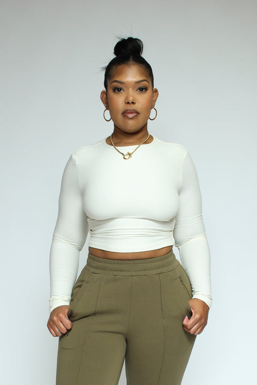 Curvy black woman wearing a white top and olive green pants on a white background